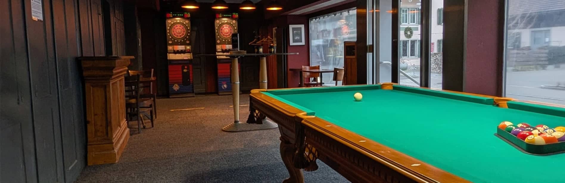Billardtisch mit grünem Filz im Magic Max Wetzikon, mit Dartscheiben im Hintergrund