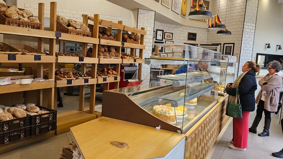 Innenansicht der deutschen Bäckerei in Málaga mit Holzregalen voller Brot, Glasvitrinen mit Gebäck und Kunden, die am Tresen bedient werden.